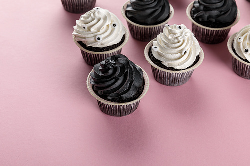 delicious Halloween cupcakes with white and black cream on pink background