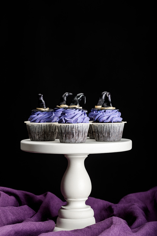tasty Halloween cupcakes on white stand on purple cloth isolated on black