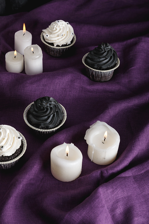 tasty Halloween cupcakes near burning candles on purple cloth