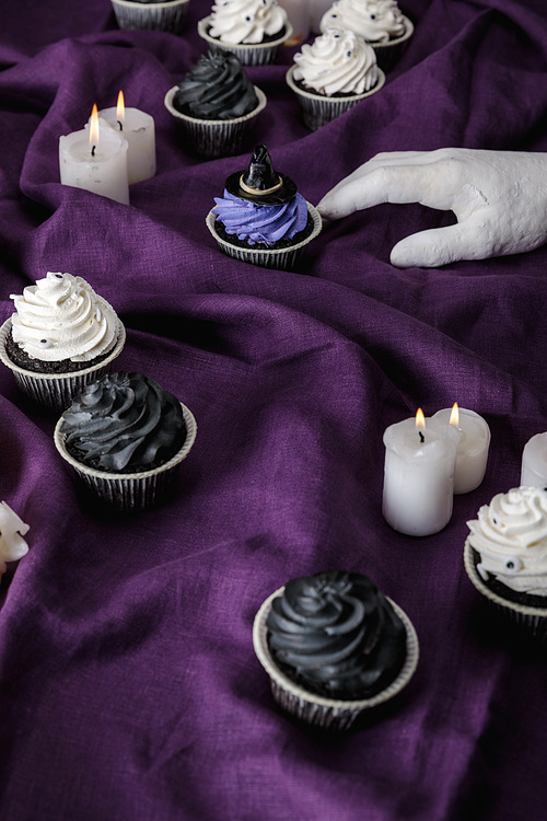decorative hand near tasty Halloween cupcakes and burning candles on purple cloth