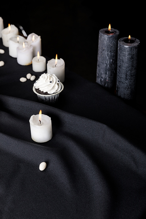 tasty Halloween cupcake with white cream near burning candles on black background