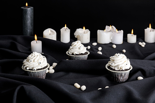 tasty Halloween cupcakes with white cream near burning candles isolated on black