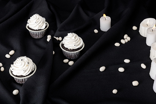 tasty Halloween cupcakes with white cream near burning candles on black cloth