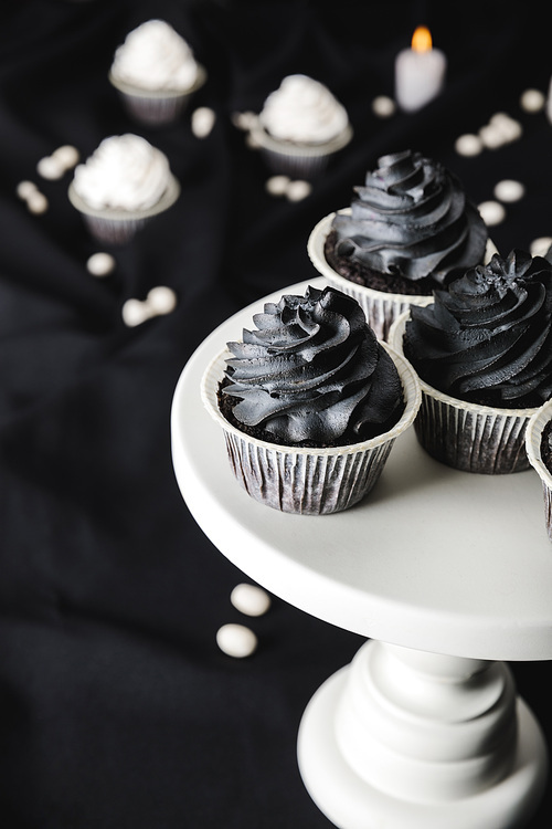 selective focus of tasty Halloween cupcakes with black cream on stand near burning candles