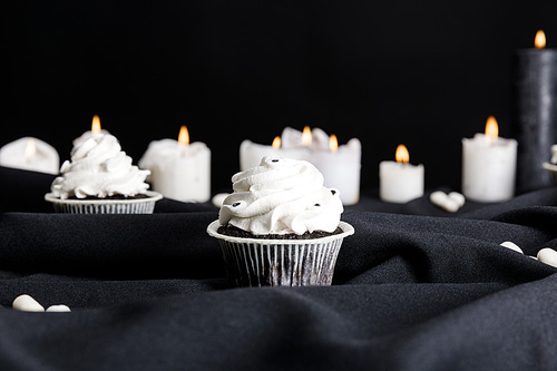 selective focus of tasty Halloween cupcakes with white cream near burning candles isolated on black