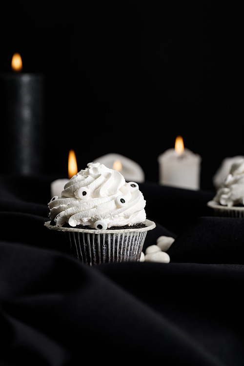 selective focus of delicious Halloween cupcake with white cream near burning candles isolated on black