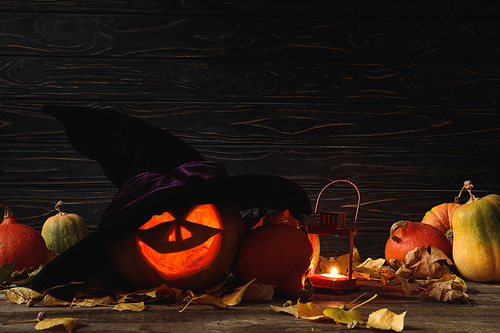 carved spooky Halloween pumpkin, autumnal leaves and burning candle on wooden rustic table on black background