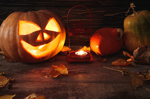carved spooky Halloween pumpkin, autumnal leaves and burning candle on wooden rustic table