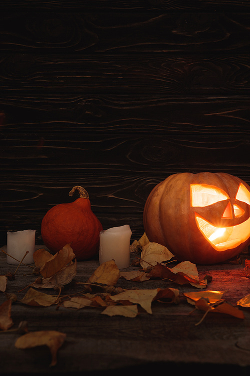 carved spooky Halloween pumpkin, autumnal leaves and candles on wooden rustic table