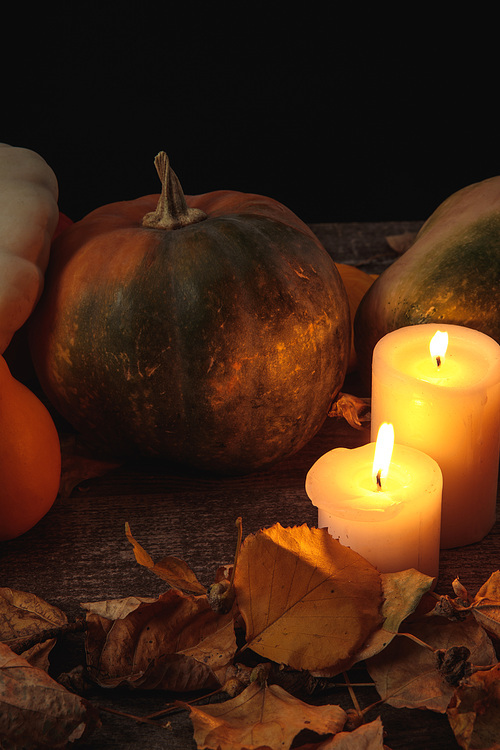 dry foliage, burning candles, ripe pumpkin on wooden rustic table isolated on black