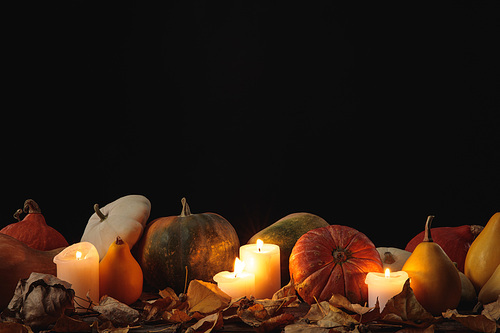 dry foliage, burning candles, ripe pumpkin on wooden rustic table isolated on black
