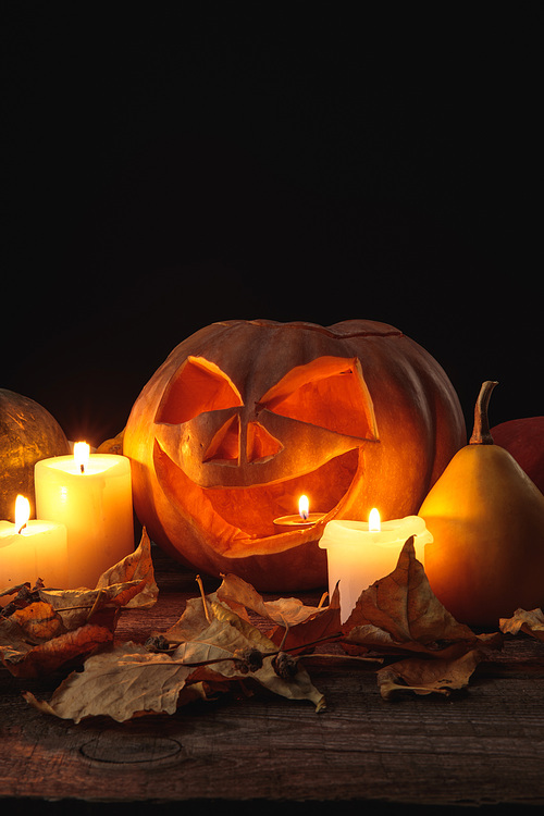 dry foliage, burning candles and Halloween carved pumpkin on wooden rustic table isolated on black