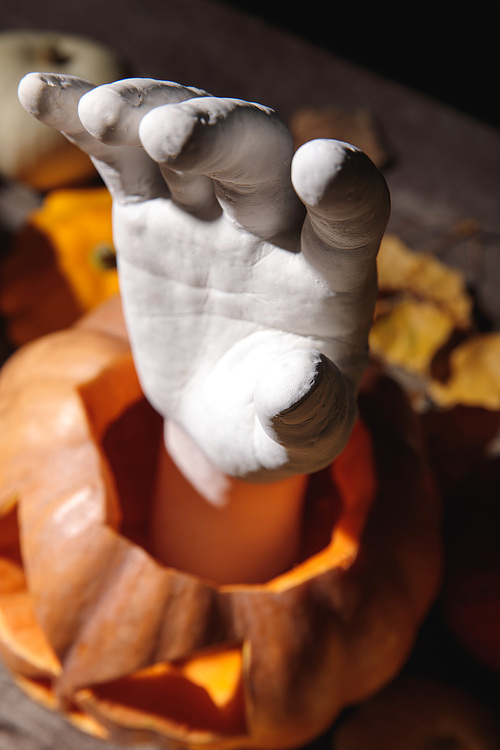 selective focus of decorative hand in carved Halloween pumpkin on wooden rustic table