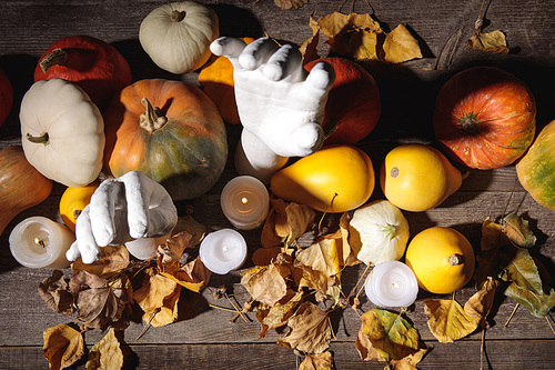 top view of dry foliage, burning candles, ripe pumpkin and decorative hands on wooden rustic table