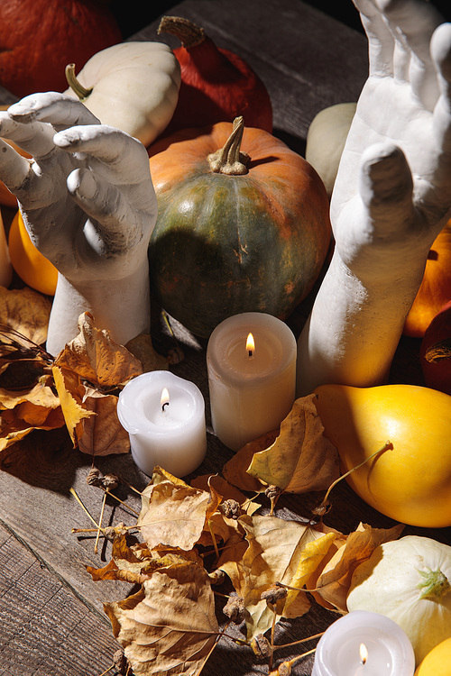 dry foliage, burning candles, ripe pumpkin and decorative hands on wooden rustic table