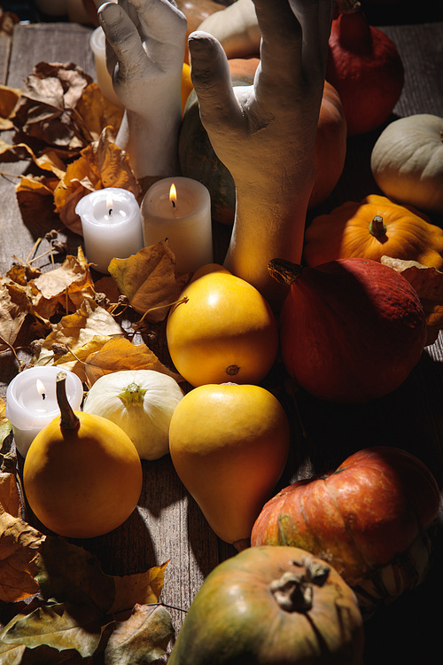 dry foliage, burning candles, ripe pumpkin and decorative hands on wooden rustic table
