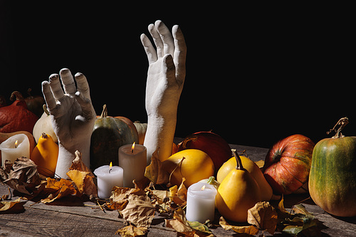 dry foliage, burning candles, ripe pumpkin and decorative hands on wooden rustic table isolated on black