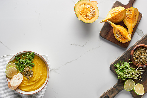 top view of tasty mashed pumpkin soup on wooden cutting board with ingredients on marble surface