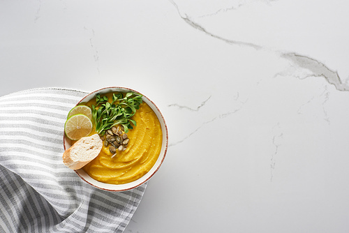 top view of tasty mashed pumpkin soup near striped napkin on marble surface
