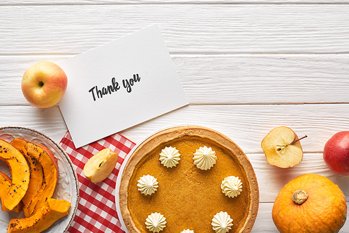 top view of pumpkin pie with thank you card on wooden white table with apples