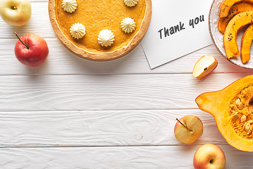 top view of delicious pumpkin pie with thank you card on wooden white table with apples