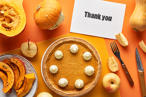 top view of delicious pumpkin pie with thank you card on orange background with apples