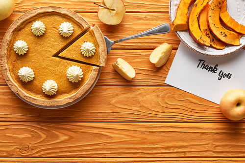 top view of pumpkin pie with thank you card on wooden table with apples