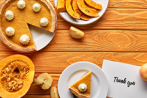 top view of pumpkin pie with thank you card on wooden table with apples