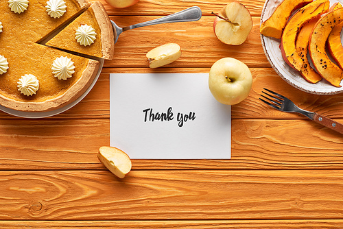 top view of delicious pumpkin pie, apples and thank you card on wooden orange table