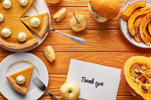 top view of delicious pumpkin pie, apples and thank you card on wooden orange table