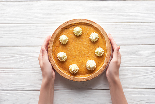 cropped view of female hands near tasty pumpkin pie with whipped cream on white wooden table