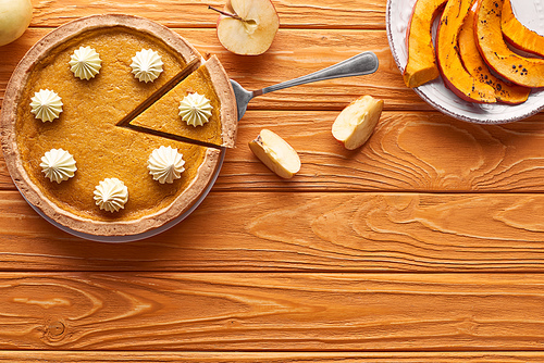 delicious pumpkin pie with whipped cream near cut apple, and sliced baked pumpkin on orange wooden table