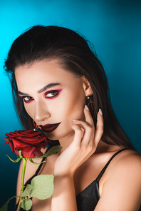 young woman with dark makeup near red rose on blue