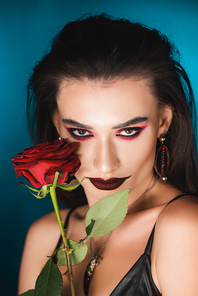 young woman with dark makeup  near red rose on blue