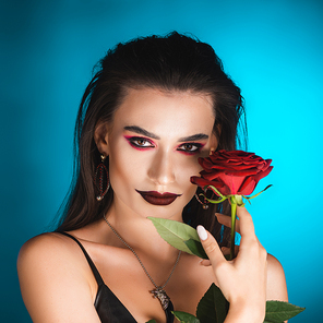 young woman with black lipstick holding red rose on blue