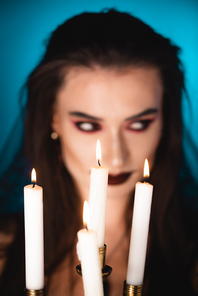 selective focus of burning candles near woman with black makeup on blue