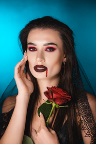 young woman in veil with blood on face holding red rose on blue