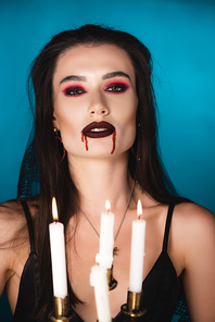 selective focus of woman with red blood on face near burning candles on blue