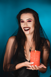 woman in veil with blood on face holding red burning candle and laughing on blue