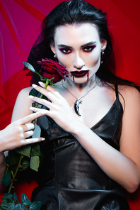 young pale woman with blood on face holding rose on red