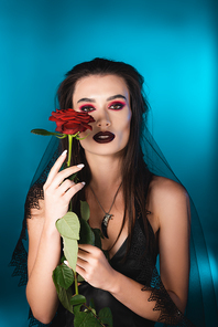 brunette woman with dark makeup holding red rose on blue