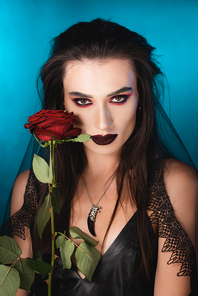 young brunette woman with dark makeup near red rose on blue