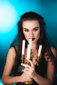 pale woman with black makeup holding burning candles on blue