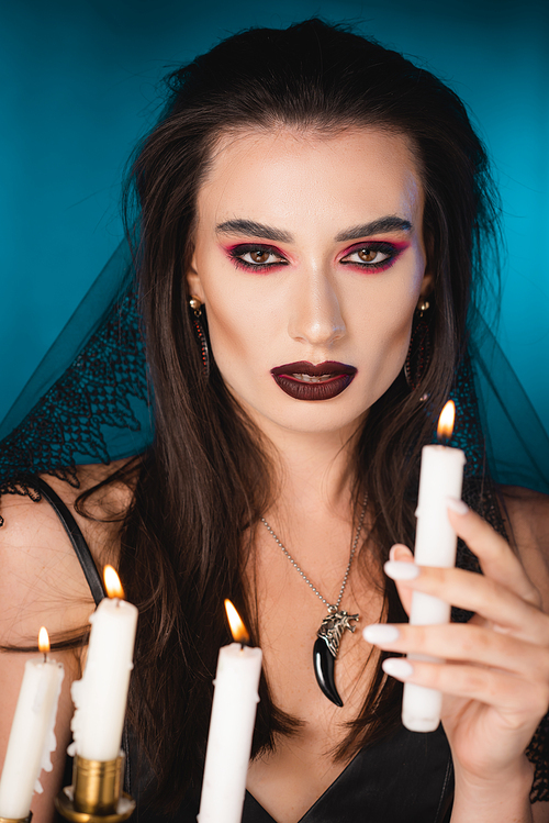 selective focus of pale young woman with makeup holding burning candle on blue