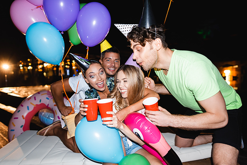 Selective focus of women clinking with disposable cups near balloons during party near swimming pool at night