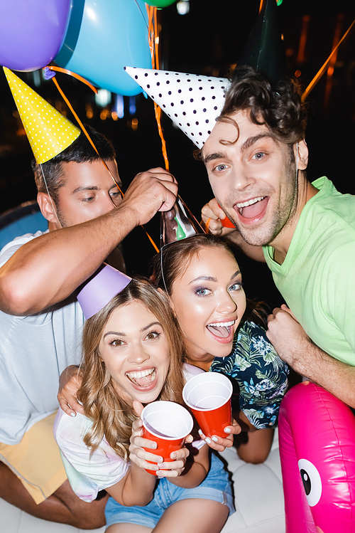 Selective focus of friends with disposable cups  near balloons outdoors at night