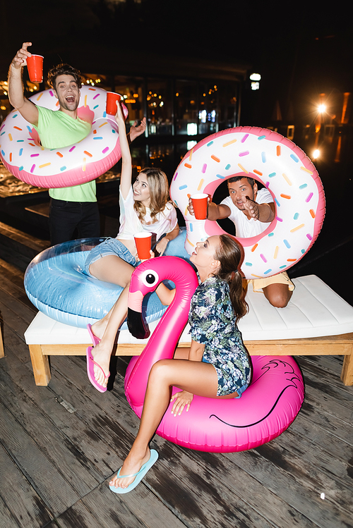 Young friends with swim rings holding disposable cups during party at night