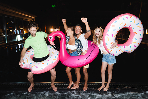 Young people dancing with swim rings near swimming pool at night