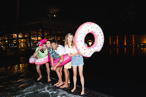 Excited young friends with swim rings  during party near pool at night