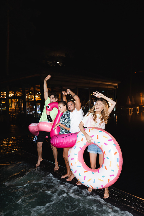 Friends dancing with swim rings during party near swimming pool at night